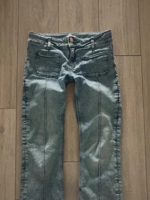 Blå låg midja bootcut jeans frpn Gina Tricot - Snygga blå jeans med utsvängda ben och markerade sömmar framtill. Jeansen har två stora fyrkantiga fickor fram och dubbla knappar i midjan. Perfekta för en avslappnad och trendig look.