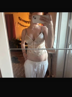 Silvrigt satinlinne med spetsdetaljer - Snyggt loungewear-linne i silvrigt satinmaterial med tunna axelband och dekorativ rosett framtill. Nederkanten har fina spetsdetaljer. 