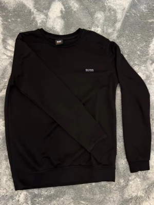 Svart sweatshirt från BOSS Storlek S - Snygg svart sweatshirt från BOSS med diskret logga på bröstet. Klassisk rund halsringning och långa ärmar. Perfekt basplagg för en clean och stilren look. Mjuk och bekväm kvalitet. Storlek S