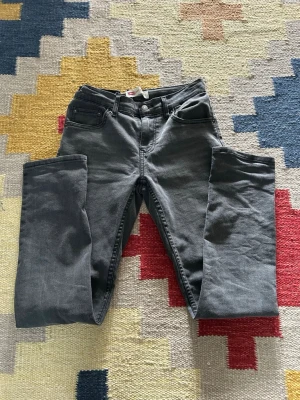 Grå jeans från Levi's - Säljer ett par grå jeans från Levi's med klassisk femficksdesign och raka ben. Jeansen har normal midja och är tillverkade i mjukt denimtyg med stretch för extra komfort. Perfekta för en avslappnad och stilren look.