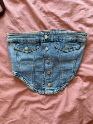 Ljusblå denim bandeau från Gina Tricot  - Unik bandeau i ljusblå denim med knappar framtill och två dekorativa fickor med lock. Snygg och edgy accessoar som ger en cool touch till din outfit. Perfekt för dig som gillar att sticka ut med detaljer i jeansmaterial. Knappt använd