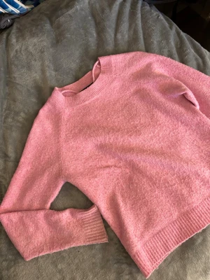 Rosa stickad tröja från Vero Moda - Mysig rosa stickad tröja från Vero Moda med rund halsringning och ribbade muddar vid ärmslut och nederkant. Perfekt för att hålla värmen under kyliga dagar och passar till många olika outfits.