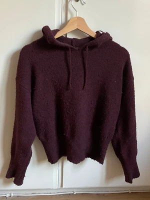 Vinröd hoodie i teddy-material - Mysig vinröd hoodie med huva och dragsnören. Tillverkad i ett fluffigt teddy-liknande material som ger en avslappnad och trendig look. Perfekt för dig som gillar oversized och bekväma plagg. Långa ärmar och rak passform.