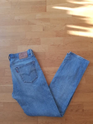Levi's 511 - Säljer ett par klassiska blå Levi's jeans med rak passform och hög midja. Jeansen har den ikoniska läderpatchen bak och en röd Levi's-tagg på bakfickan. Perfekta för dig som gillar vintage vibe och tidlös denimstil.