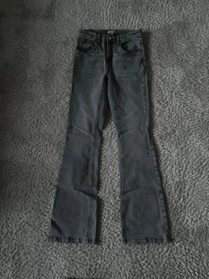 Grå bootcut jeans med medelhög midja - Snygga grå jeans med bootcut-modell och medelhög midja. Klassisk femficksdesign och knappgylf. Jeansen har en tvättad look och är tillverkade i ett mjukt denimtyg som ger en avslappnad vibe. Barn storlek 170 men passar som en xxs. Aldrig använda.