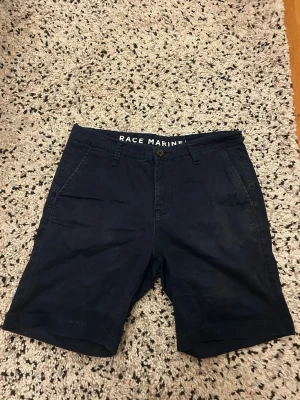 Marinblå shorts från Race Marine - Snygga marinblå shorts från Race Marine med klassisk passform. Shortsen har två sidofickor fram och två bakfickor med knappdetalj. Tillverkade i bomull för en skön känsla och stilren look. Perfekta för varma dagar.