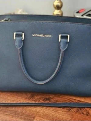 Michael Kors Selma medium  - Snygg mörkblå handväska från Michael Kors i modellen Selma i storlek Medium. Den är gjord i  strukturerat läder med guldfärgade detaljer och dragkedja. Väskan har både handtag och en lång axelrem för olika stilar. Perfekt för dig som vill ha en klassisk och stilren accessoar.