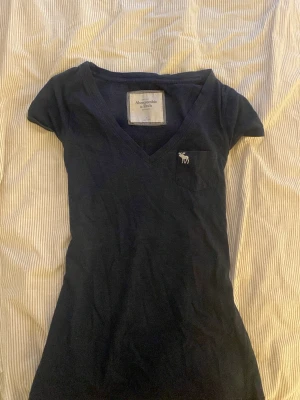 Svart v-ringad t-shirt Abercrombie - Svart v-ringad t-shirt från Abercrombie & Fitch med liten bröstficka och broderad logga. T-shirten är kortärmad och har en slim passform. Tillverkad i mjuk bomull som känns skön mot huden.