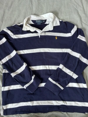 Ralph Lauren seglar tröja - Mörkblå och vit långärmad rugby/seglar tröja från  Ralph Lauren ränder, klassisk vit krage och gul broderad logga på bröstet. Tillverkad i bomull och har en relaxed passform. Storlek XL sitter mer som L. Tveka inte o skriv för frågor etc ✨✨🎶🎶🎶