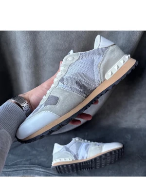 Valentino rock runners - Snygga rock runners från Valentino i nyanser av grått och vitt. Skorna har en mix av mocka, mesh och läderdetaljer samt den ikoniska nitarna på hälen. Yttersulan är svart med beige mellansula för en clean look. Tygen inne vid sulan är lite trasigt annars är inget sönder 