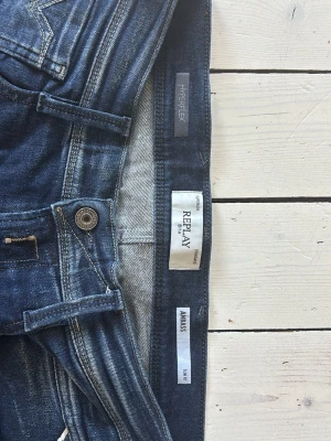 Mörkblå slim fit jeans från Replay - Snygga mörkblå jeans från Replay i modellen Anbass med slim fit-passform. Jeansen har klassisk femficksdesign, dragkedjegylf och coola slitningar. Perfekta för dig som gillar en modern och stilren look. Köpt för 1299kr!