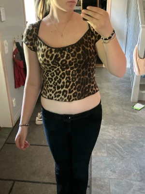 Leopardmönstrad croppad topp - Snygg croppad topp med leopardmönster och korta ärmar. Toppen har en tight passform och en liten spetsdetalj vid halsringningen. Perfekt för dig som vill se fin ut med ett djurmönster. 
