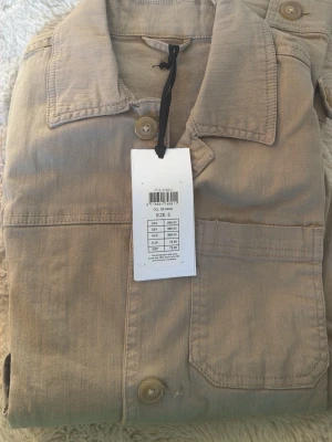 Beige skjorta från Lindbergh - Stilren beige skjorta från Lindbergh med klassisk krage och bröstficka. Skjortan har knäppning framtill och är tillverkad i ett mjukt bomullstyg. Perfekt för en clean och avslappnad look. 