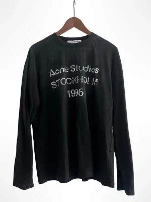 Svart långärmad Acne Studios - Svart långärmad topp från Acne Studios med vit text 'Acne Studios STOCKHOLM 1996' framtill. Klassisk rund halsringning och rak passform. Perfekt för en clean och stilren look. Priset kan såklart diskuteras vid en snabb affär🤝✅