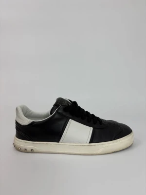 Valentino flycrew sneakers - Snygga sneakers från Valentino i svart och vitt skinn. Klassisk låg modell med svarta snören och vit sula med små nitar baktill. Perfekta för dig som vill ha en stilren men ändå edgy look.