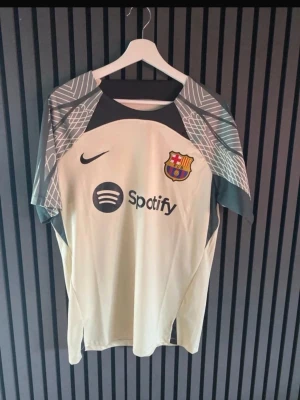 Barcelona matchtröja Nike beige - Säljer en beige FC Barcelona matchtröja från Nike med klubbmärke och Spotify-logga på bröstet. Tröjan har gråmönstrade ärmar och svart Nike-logga. Perfekt för dig som älskar fotboll och vill ha en snygg supportertröja.