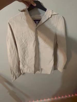 Beige skjorta med krage org pris: 599kr - Säljer en stilren beige skjorta med klassisk krage och långa ärmar. Skjortan är enkel och passar perfekt till många olika outfits. Tillverkad i ett mjukt bomullsmaterial för en bekväm känsla.