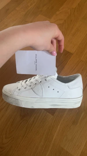 Vita Philippe Model sneakers - Stilrena vita sneakers från Philippe Model med klassisk låg siluett. Skorna har ovandel i läder, vita snören och diskreta detaljer som perforeringar och märkets logotyp på sidan. Tjock vit sula ger en modern touch. Perfekta för en clean och trendig look. Skorna är helt nya med prislapp, orginal pris 3500kr, mitt pris går att diskutera.