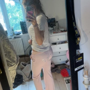 Ljusrosa Juicy Couture mjukisbyxor XXS - Säljer ett par ljusrosa mjukisbyxor från Juicy Couture i storlek XXS. Byxorna har raka ben, låg midja och glittrig Juicy-text baktill. Mjukt material och klassisk Y2K-vibe, perfekta för en chill och trendig look. Den har också en fläck på höger ben, så jag råder dig till att vara lite kortare o sen sy upp dom, men annars så funkar dom ju ändå. Jag har också sytt in dom, jag är en 15åring tjej och är 158 cm lång, dom sitter perfekt på mig i midjan men dom är aldelds för långa. 
