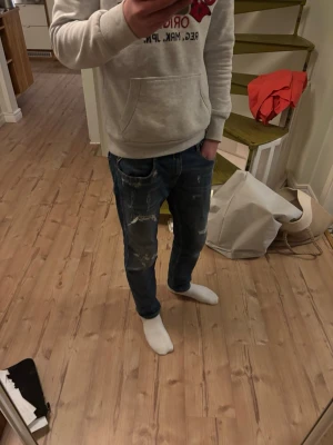 Replay ambass - Säljer ett par blåa jeans från replay med slitningar och distressed detaljer på benen. Klassisk femficksmodell med slim fit och läderpatch bak i midjan. Perfekta för en avslappnad och trendig look. Modell: Replay ambass