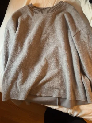 Grå oversized stickad tröja Zara - Mysig grå stickad tröja från Zara. Tröjan har rund halsringning med bred ribbstickad kant och långa ärmar. Perfekt för lager-på-lager och chill dagar. Tillverkad i mjukt material som känns skönt mot huden.