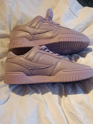 Ljuslila sneakers från FILA - Snygga ljuslila sneakers från FILA i klassisk low-modell. Skorna är tillverkade i slätt syntetläder med matchande lila sula och detaljer. Perfekta för dig som vill sticka ut med en unik färg på dina sneakers.