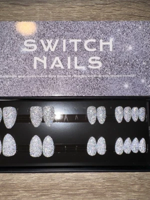 Switch Nails Silver Flash press-on - Glittriga press-on naglar i modellen Silver Flash från Switch Nails. Naglarna har en kort mandelform och är täckta av silvrigt glitter som verkligen poppar. Perfekt för dig som vill ha snygga och trendiga naglar snabbt. Gjorda av återvunnet material. Säljes utan tillbehör.