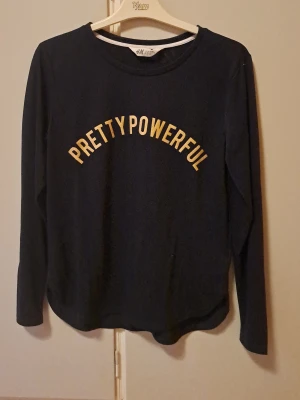 Långärmad topp H&M barbie popstar - Navy unik långärmad topp från H&M med rund halsringning och texten 'PRETTY POWERFUL' i glittrande guldfärg. Cool färg comb guld o blå. Tillverkad i mjuk bomullsmix som känns skön mot huden. Perfekt för dig som vill ha en enkel men statement vardagstopp. Fin desgin/cut nertill. Storlek 170 men känns som XS/S. 2000s barbie popstar