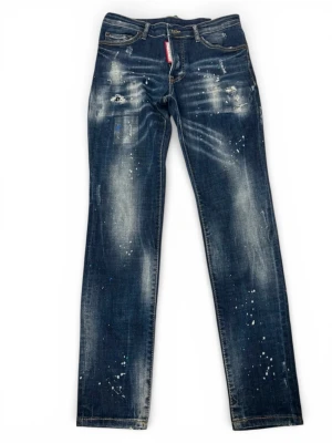 Mörkblå distressed jeans Dsquared2 - Säljer ett par mörkblå jeans från Dsquared2 med slitningar, färgstänk och en rak passform. Jeansen har klassiska fem fickor, synliga sömmar och en cool vintage look. Perfekta för dig som gillar streetwear och unika detaljer.