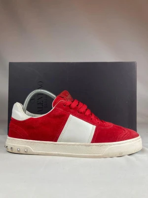 Valentino Flycrew - Snygga röda sneakers från Valentino Garavani i mocka med vita detaljer och vita sulor. Skorna har klassisk låg profil, röda skosnören och små nitar på hälen. Perfekta för dig som vill sticka ut med stilrena och exklusiva sneakers. Storlek 40 men passar 41