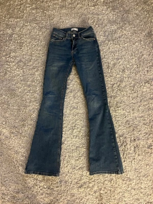 Mörkblå bootcut jeans - Ett par mörkblå bootcut jeans med klassisk femficksdesign. Jeansen har normal midja och utsvängda ben, perfekta för en trendig och avslappnad look. Tillverkade i denim med snygga kontrastsömmar.