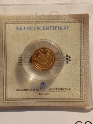 Guldfärgad minnesmynt med certifikat - Unik guldfärgad minnesmynt från Skandinavisk Myntkontor, levereras i plastkapsel med äkthetscertifikat. Myntet har detaljerat motiv och latinsk text runt kanten. Perfekt för samlare eller som present till någon som gillar historia och mynt. 14 karat guld (58.50% guld).