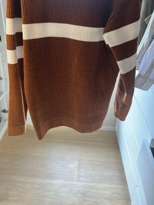 Brun stickad tröja med vita ränder - Snygg brun stickad tröja med vita horisontella ränder över bröstet och på ärmarna. Tröjan har ribbad struktur och långa ärmar. Perfekt för dig som gillar retrovibbar och vill ha något bekvämt och stilrent i garderoben. Storlek L, passar nästan bättre som M skulle jag säga. Inget tecken på användning, den är använd max 3 gånger skulle jag säga. Säljer då jag behöver lite pengar och har för mycket kläder. Köpte den för 1399kr när jag va Italien. Nu får ni den för 800kr spikat pris då den är oanvän