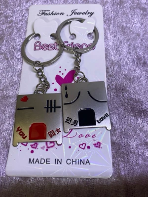 Best Friends nyckelringsset metall - Unikt nyckelringsset i metall med två delar som passar ihop, dekorerade med svarta och röda detaljer samt texten 'you', 'love' och kinesiska tecken. Perfekt för att dela med en vän. Silverfärgade med hjärtmotiv och roliga figurer.