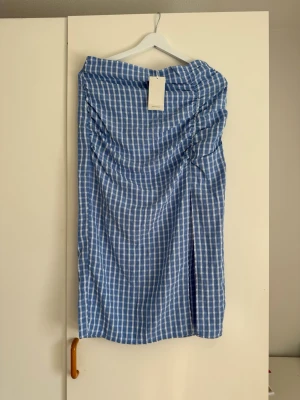 RESERVED blå midi kjol, storlek EUR 40 - En blå och vit rutig kjol med en elegant slits framtill. Kjolen har en smickrande rynkad detalj på ena sidan som ger en fin drapering. Den stängs med en diskret dragkedja baktill.  Buy shipping label or pick it up from Farsta centrum in Stockholm.