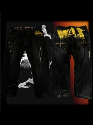 Svarta jeans från Wax Actionwear - Säljer ett par svarta jeans från Wax Actionwear med slitna detaljer och coola gula tryck på bakfickorna. Jeansen har raka ben och tydliga slitningar framtill för en edgy streetstil. Perfekta för dig som gillar unika och uttrycksfulla plagg.