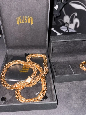 Guldfärgat armband från Kejsar - Snyggt guldfärgat halsband från Kejsar med flätad kedja och rektangulärt lås med stenar. Den är 65cm lång med 8mm bredd och levereras i original ask. Perfekt accessoar för att lyfta din outfit.  Köpt för 2799kr men priset kan disskuteras vid snabba köp 