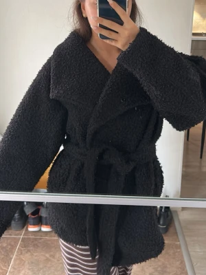 Svart teddyjacka med knytskärp - Mysig svart teddyjacka med oversized krage och knytskärp i midjan från ginatricot. Jackan har dubbelknäppning framtill och är gjord i fluffigt teddy-material. Perfekt för kyliga dagar 🖤