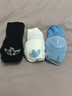 Adidas strumpor svart, vit & blå - Tre par Adidas strumpor i svart, vit och ljusblå. Klassisk modell med ribbad struktur, Adidas-logga på sidan och två ränder upptill. Perfekta för dig som gillar sportig stil och vill ha bekväma strumpor med snygg design.