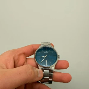 Silverfärgad klocka med blå urtavla - Stilren klocka från MORRIS med blå urtavla och datumvisning. Armbandet är i silverfärgad metall och klockan har en klassisk rund form. Perfekt accessoar för dig som gillar en clean och modern look.