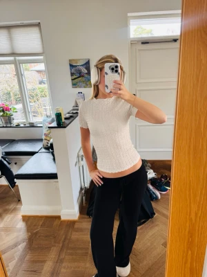 Vit Zara topp med kort ärm - Säljer en vit topp med smockad struktur och korta ärmar. Toppen har en kroppsnära passform och lätt vågig kant nedtill. Perfekt för dig som gillar en enkel men trendig stil.