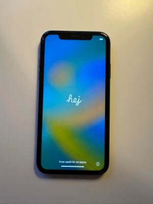 Svart iPhone XR med glasbaksida - Säljer en svart iPhone XR med stilren design och rundade kanter. Telefonen har en stor skärm med tunn ram och baksida i glas med Apple-loggan. Perfekt för dig som gillar snygg och enkel mobil.