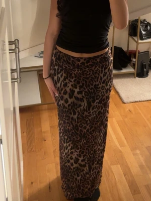 Lång leopardmönstrad kjol - Säljer en lång kjol med leopardmönster i bruna och svarta toner. Kjolen har en rak passform och sitter snyggt i midjan. Perfekt för dig som vill sticka ut med ett djurmönster i garderoben. (Aldrig använt) 