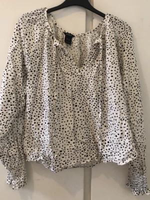 Vit prickig blus  - Snygg vit blus från Lindex med svarta prickar, v-ringning och långa ärmar med smockade muddar. Blusen har en luftig passform och är gjord i ett lätt tyg som känns skönt mot huden. Skriv priv om du vill se den på, pris kan diskuteras ❤️