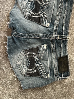 Blå jeansshorts från big star - Säljer ett par blå jeansshorts från Big star med slitna kanter och kontrastsömmar. Shortsen har stora bakfickor med broderade detaljer och en klassisk femficksdesign. Perfekta för sommaren och ger en cool, avslappnad look. Köpte på vinted.