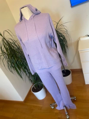 Ljuslila ribbat loungewear-set - Mysigt loungewear-set i ljuslila ribbat material. Setet består av en hoodie med dragsko och matchande byxor med utsvängda ben med slits på sidor