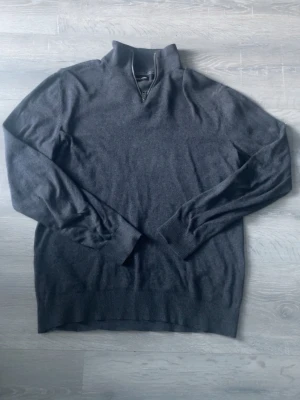 Mörkgrå quarterzip Jack & Jones - Mörkgrå stickad tröja från Jack & Jones i storlek M. Tröjan har en half zip-dragkedja vid halsen och är långärmad med ribbade muddar. Perfekt till höst och vinter för en clean och enkel look.