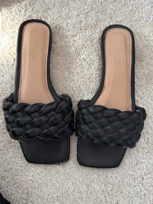 Svarta flätade sandaler med fyrkantig tå - Snygga svarta sandaler med bred, flätad rem i konstläder och fyrkantig tå. Innersulan är beige och har en lätt vaddering för extra komfort. Perfekta för en trendig och stilren look.