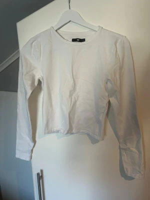 Vit figursydd långärmad topp - Säljer en enkel och stilren vit långärmad topp från Bikbok. Modellen är croppad med rund halsringning och har en tight passform. Perfekt att matcha med höga jeans eller kjol för en clean look.