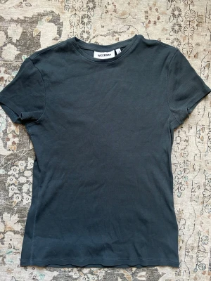 Mörkblå ribbad t-shirt från Weekday - En enkel och stilren mörkblå t-shirt från Weekday med ribbad struktur. T-shirten har korta ärmar och rund halsringning, perfekt för en avslappnad look. Materialet är mjukt och bekvämt, vilket gör den lätt att bära hela dagen.